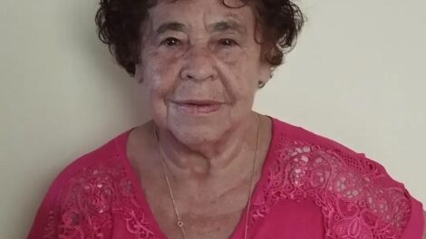 a foto mostra uma ideosa de 70 anos com blusa rosa, cabelos encaracolados e semblante levemente sorrindo